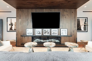 Ein modernes Wohnzimmer mit großem Flachbildfernseher, einer Holzwandverkleidung, gerahmten Kunstwerken und Couchtischen mit Marmorplatten.