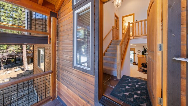 Een houten chalet met een trap die naar een bovenverdieping leidt, een balkon met een leuning, en een deur met een welkomstmat.