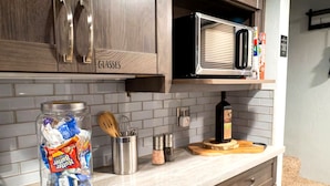 Una cocina con armarios de madera, microondas, especiero y un tarro de aperitivos.