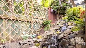 Un jardín con una pequeña cascada, una cerca de madera y diversas plantas.