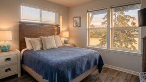 A bedroom with a bed, two bedside tables, a ceiling fan, and two windows.