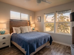 Ein Schlafzimmer mit einem Bett, zwei Nachttischen, einem Deckenventilator und zwei Fenstern.