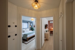 Un pasillo que conduce a un dormitorio con cama, mesita de noche y televisor instalado en la pared.