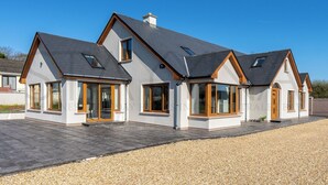 Une maison moderne à deux étages, dotée d’un toit en pente, de grandes fenêtres et d’une allée gravillonnée.