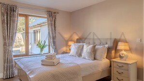 Une chambre à coucher avec un lit, des tables de chevet, une fenêtre avec des rideaux et une vue sur l’extérieur.