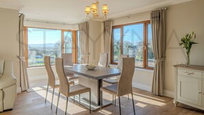 Un espace repas comprenant une table, des chaises, un lustre et de grandes fenêtres avec des rideaux.