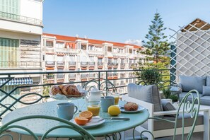 Ein Balkon mit Frühstückstisch, mit Croissants, Orangensaft und einem Muffin, mit Blick auf eine Reihe von Gebäuden mit Balkonen.