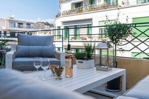 Eine Terrasse mit einer Couch, zwei Weingläsern, einer Flasche, einer Oliven-Schale und einem Blumentopf.