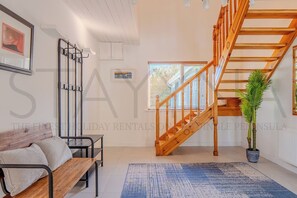 Ein modernes Wohnzimmer mit einer Holztreppe, einem Sofa, einem Couchtisch und einer Topfpflanze.