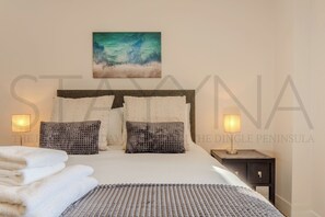 Ein Schlafzimmer mit Bett, Kissen, Decke, Nachttisch, Lampe und einem Bild an der Wand.