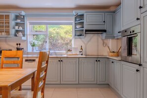 A kitchen with white cabinets, a window, a dining table, and a chair.