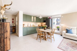 Una cocina moderna con armarios verdes, un área de comedor con sillas de madera y una sala de estar con sofá y lámpara.