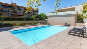 Ein Schwimmbecken mit Liegestühlen und ein Gebäude mit Balkonen im Hintergrund.