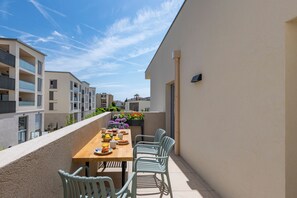 A balcony with a wooden table set for breakfast, surrounded by light blue chairs, and overlooking a residential area. - Bellevue Flora 2 bedroom apartment (Antibes)