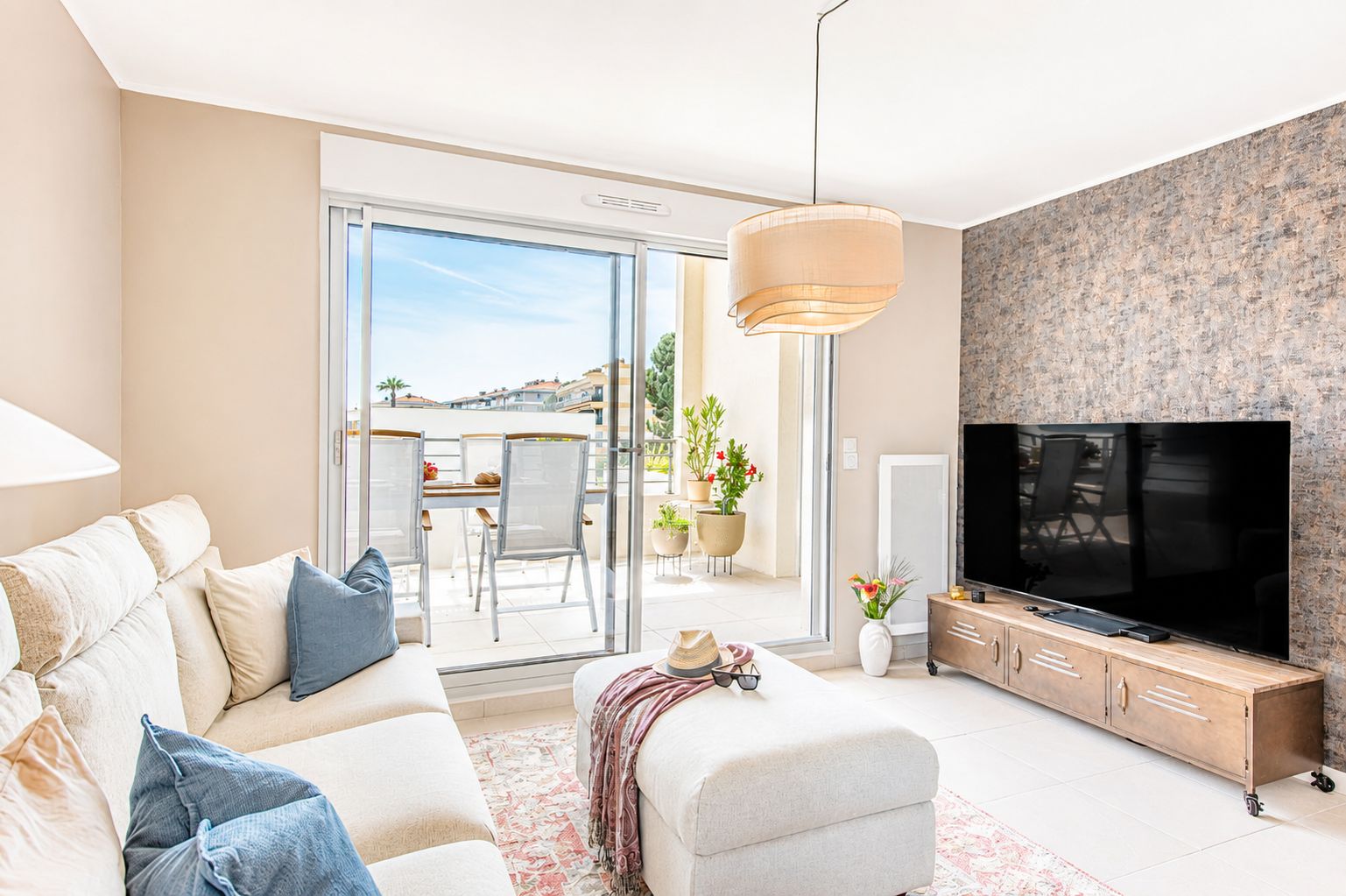 A modern living room with a sofa, TV, and a balcony with outdoor furniture.