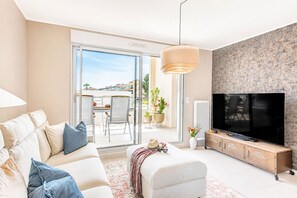 Ein modernes Wohnzimmer mit Sofa, Fernseher und einem Balkon mit Gartenmöbeln.