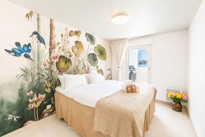 A hotel room with a bed, a large wall mural, a window, and a small table with towels. - Bellevue Flora 2 bedroom apartment (Antibes)