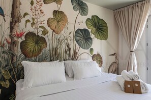 Ein Hotelzimmer mit einem Bett, weißen Kissen, einem tropischen Wandbild und einer Vogelstatue.