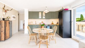 Eine moderne Küche mit grünen Schränken, einem schwarzen Kühlschrank und einem Essbereich mit einem runden Tisch und Holzstühlen.