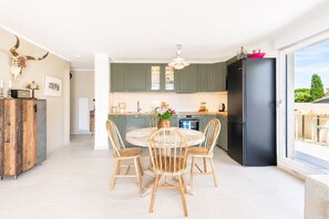 A modern kitchen with green cabinets, a black refrigerator, and a dining area with a round table and wooden chairs. - Bellevue Flora 2 bedroom apartment (Antibes)