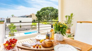 Ein Balkon mit einem Esstisch, einer Olivenölflasche und Blick auf einen Swimmingpool sowie Gebäude.