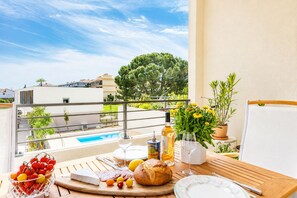 A balcony with a table set for a meal, a bottle of olive oil, and a view of a swimming pool and buildings. - Bellevue Flora 2 bedroom apartment (Antibes)