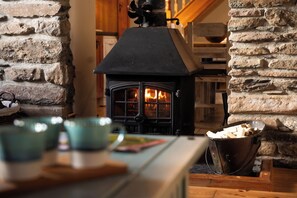 Ein Kamin aus Stein mit schwarzem Sims, ein Holztisch mit einer Holzschüssel und ein Korb.