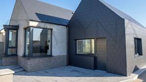 Ett modernt hus i två våningar med stora fönster, en grund av sten och ett mörkt tak.