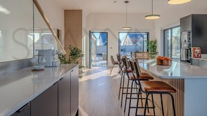 Ett modernt kök med en stor köksö, barstolar, hängande lampor och utsikt över omgivningen.