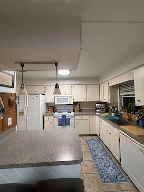 A kitchen with white cabinets, a granite countertop, a stove, a microwave, and hanging pendant lights. - Harris chain Lake House Hideaway (Tavares)