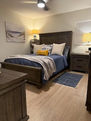 A bedroom with a wooden bed, bedside tables, a nightstand, a lamp, a rug, and a painting on the wall. - Harris chain Lake House Hideaway (Tavares)