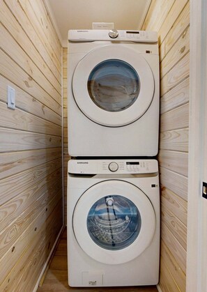 Two stacked Samsung washing machines in a wooden-paneled laundry room. - CL5 Shared Pool, Charcoal Grill, Old Town Port A (Port Aransas)