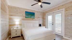A bedroom with a bed, nightstand, lamp, ceiling fan, and a painting. - CL5 Shared Pool, Charcoal Grill, Old Town Port A (Port Aransas)