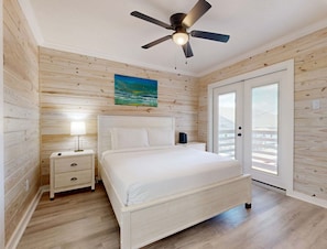 A bedroom with a bed, nightstand, lamp, ceiling fan, and a painting. - CL5 Shared Pool, Charcoal Grill, Old Town Port A (Port Aransas)