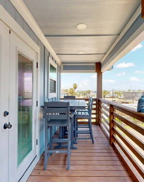 A covered outdoor deck with a table and chairs, a wooden railing, and a view of the surrounding area. - CL5 Shared Pool, Charcoal Grill, Old Town Port A (Port Aransas)