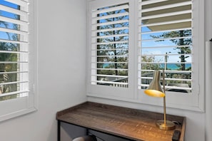 A corner room with white walls, a wooden desk, and a window with white shutters. - Beachfront 2b Home. Parking. Wifi. (Broadbeach)