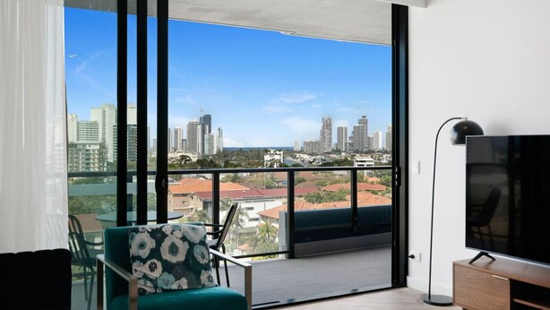 Una sala de estar moderna con un balcón grande, un televisor de pantalla plana y vistas a un horizonte urbano.