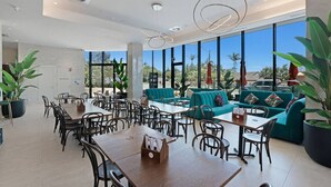 Un comedor moderno con mesas y sillas, un sofá y ventanas amplias con vistas al exterior.