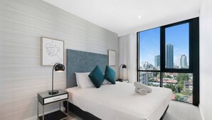 Una habitación de hotel moderna con una cama grande, dos mesitas de noche, vistas a la ciudad y una obra de arte enmarcada en la pared.