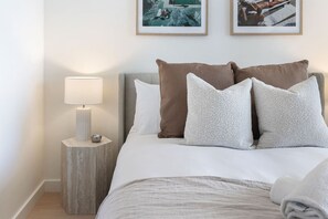 Un lit bien fait, avec du linge de lit blanc, une lampe de chevet et deux tableaux encadrés accrochés au mur.