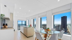 Una cocina moderna con una isla central, un comedor con mesa de vidrio y ventanas amplias que ofrecen vista a la ciudad.