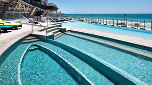 Una piscina con agua cristalina, una terraza con sillas reclinables y vista al océano.