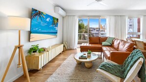 A modern living room with a sofa, coffee table, and a painting of a beach scene. - Palm Beach 3b Apartment. Parking. Wifi. (Palm Beach)