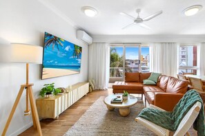 A modern living room with a sofa, coffee table, and a painting of a beach scene. - Palm Beach 3b Apartment. Parking. Wifi. (Palm Beach)