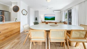A modern kitchen with a wooden countertop, a clock, and a dining area with a large table and wicker chairs. - Palm Beach 3b Apartment. Parking. Wifi. (Palm Beach)