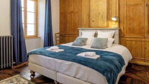 Ein Schlafzimmer mit hölzernem Kopfteil, einem großen Bett mit weißer Bettwäsche und einem Fenster mit blauen Vorhängen.