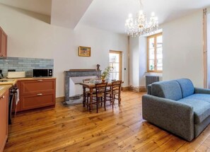 A spacious kitchen with wooden flooring, a dining area with a table and chairs, a blue sofa, and a chandelier. - Stendhal House - La Chartreuse (LES ECHELLES)