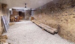 A room with a stone wall, a wooden bench, a table with chairs, and a ceiling fan. - Stendhal House - La Chartreuse (LES ECHELLES)