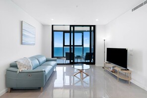 A modern living room with a sofa, a TV, a glass coffee table, and a view of the sea through large windows. - Beachfront 2b Apartment Meriton (Surfers Paradise)