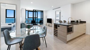 Een moderne keuken met een centraal eiland, een eetgedeelte met een glazen tafel, en een woonruimte met uitzicht op zee.